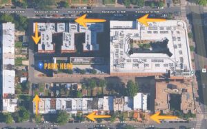 Aerial view of a city block with labeled "PARK HERE" area, orange arrows showing directions along Randolph St NW and Quincy St NW, near Luxury Apartments.